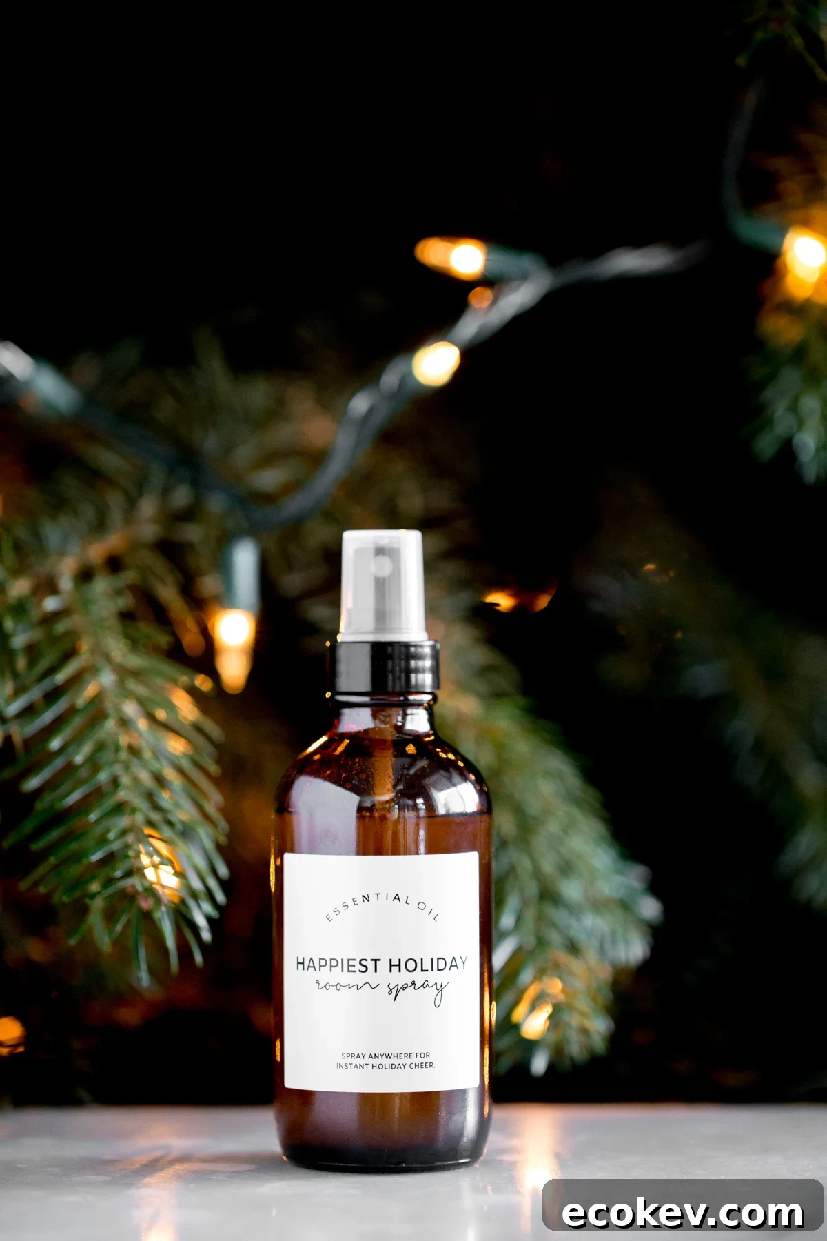 bottle of homemade DIY essential oil holiday room spray with a lit tree in the background title text overlay
