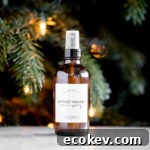 bottle of homemade essential oil holiday room spray with a lit tree in the background title text overlay