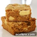 Two pieces of Caramilk Brownies on top of each other on a white bench.