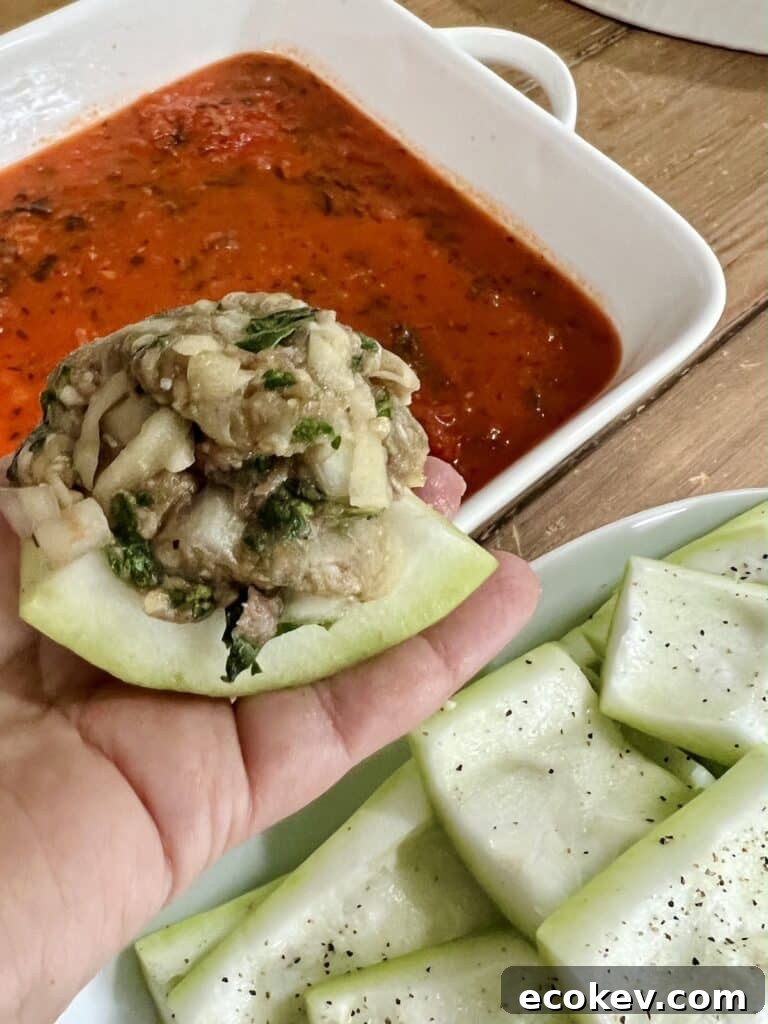 Close-up side view of one piece of stuffed cucuzza squash uncooked with a baking dish lined with marinara sauce in the background.