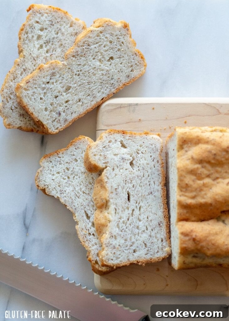 Sliced gluten-free bread next to a cutting board with a serrated knife and a whole loaf.