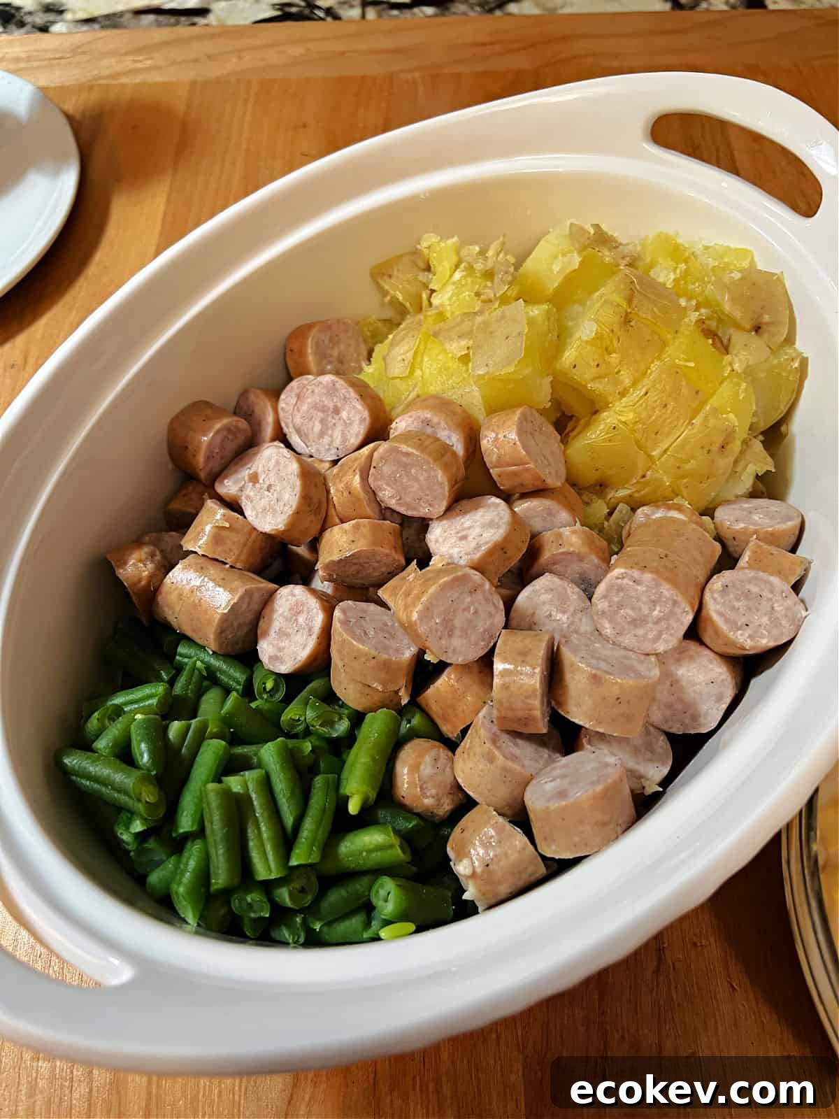 casserole ingredients in baking dish: cut up brats, potatoes, and green beans.
