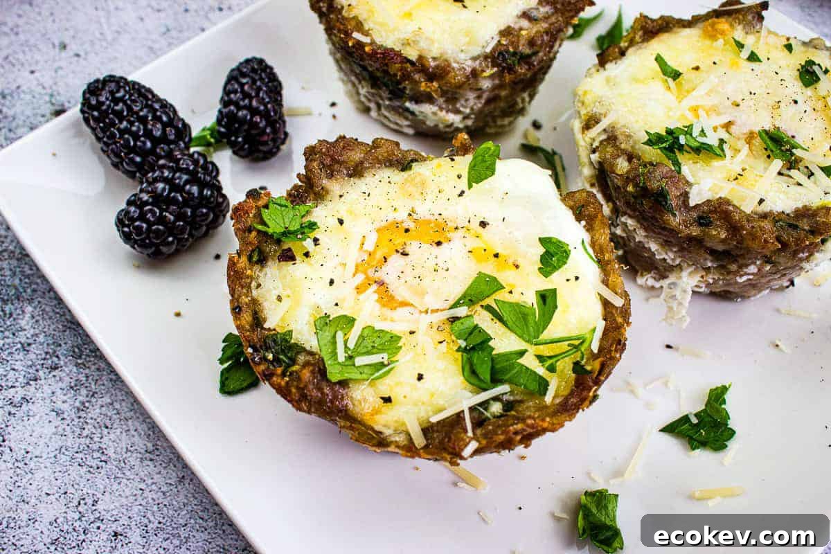 Three baked egg and meat cups topped with herbs and cheese are on a white plate, accompanied by blackberries.