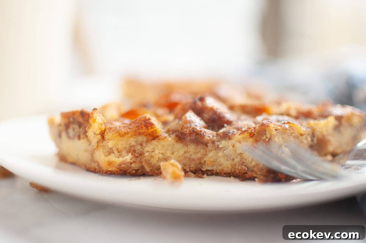 A close-up of a partially eaten piece of Cinnamon Roll Casserole on a white plate, with a fork resting beside it.