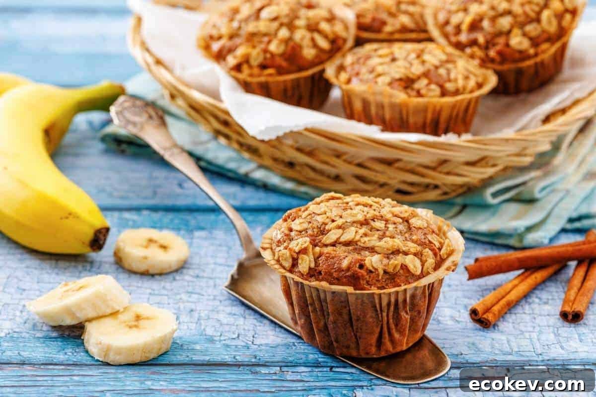 Banana oatmeal muffins on a metal spatula and in a basket, with sliced bananas and cinnamon sticks on a blue wooden surface.