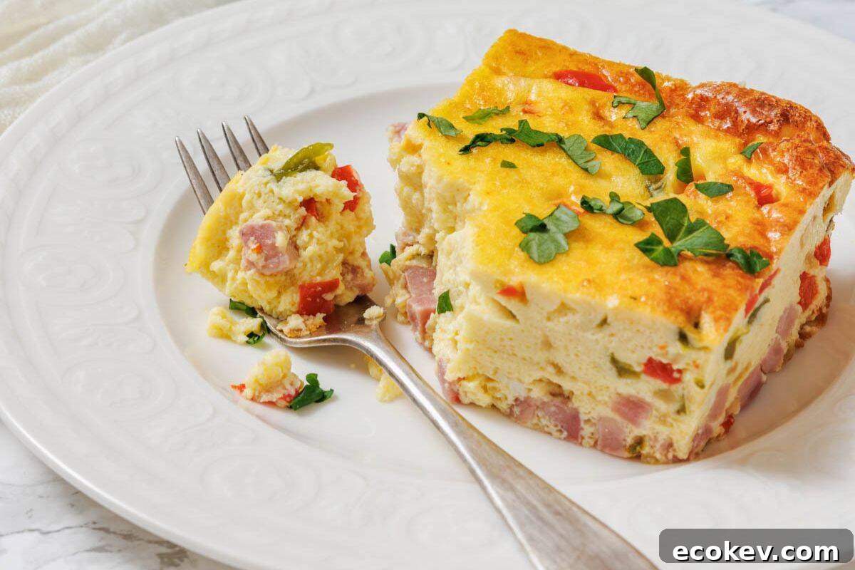 A slice of baked Western omelet with ham, red peppers, and herbs is served on a white plate with a fork holding a bite-sized piece.