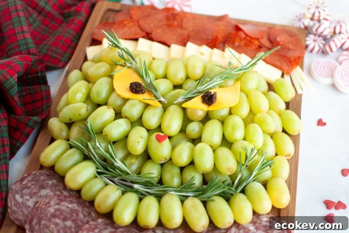 A charcuterie board arranged to resemble the Grinch's face, made with green grapes, cheese, meat slices, and garnished with rosemary.