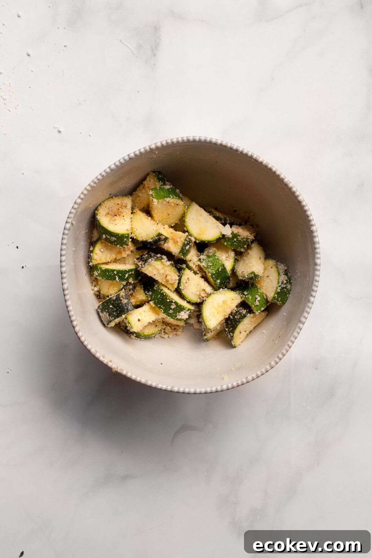 Bite-sized zucchini pieces in a mixing bowl tossed with Parmesan, garlic powder, onion powder, salt, and black pepper.