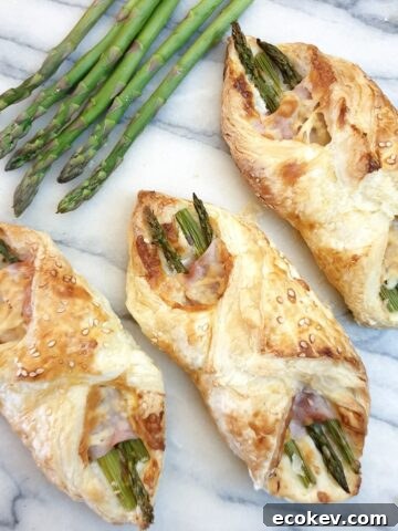 3 ham and asparagus wraps on a marble board with spears of fresh asparagus at the side.