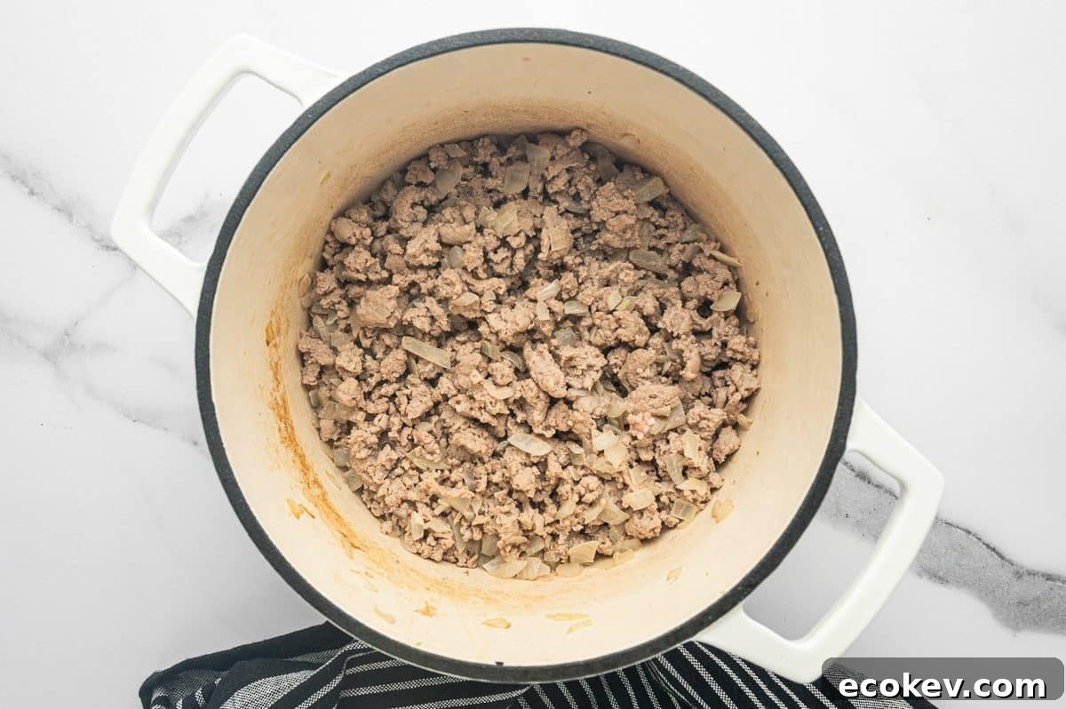 Overhead photo of browned crumbled ground turkey mixed with softened chopped onions inside a white enameled Dutch oven.