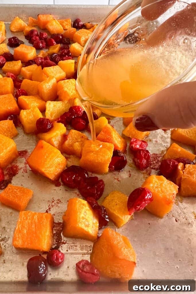 Honey being drizzled over oven roasted butternut squash and cranberries on a sheet pan.
