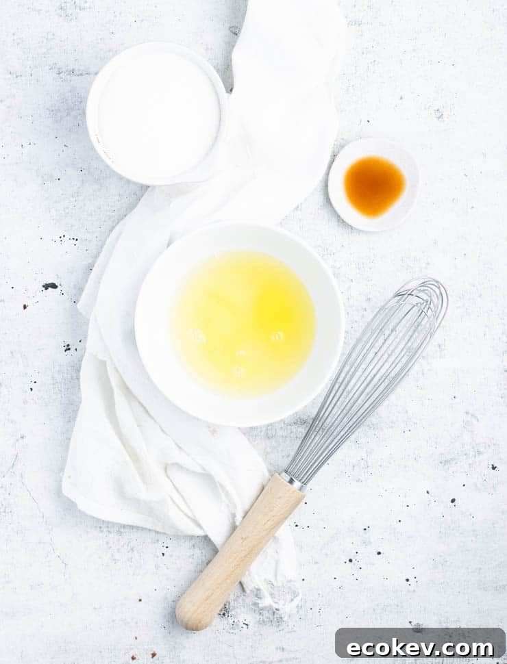 ingredients for meringue (egg white, sugar and vanilla extract) in bowls next to a whisk