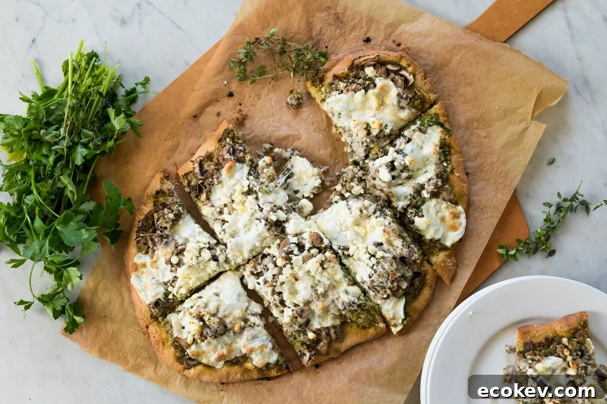 Top down view of sliced pizza sitting on wood board with piece of parchment underneath with one slice sitting on a white plate all after coming out of the oven from baking