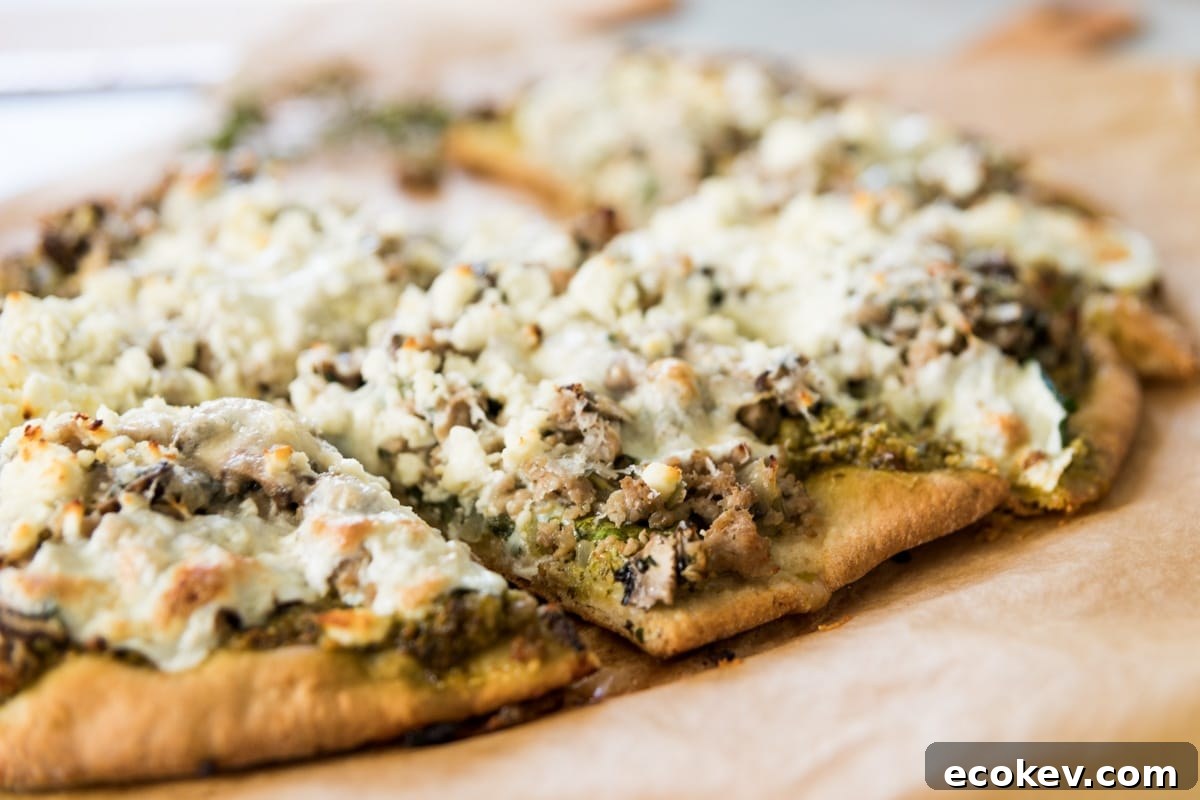 Slice of spinach pizza sitting on brown piece of parchment paper topped with sausage and crumbly feta cheese after coming out of the oven