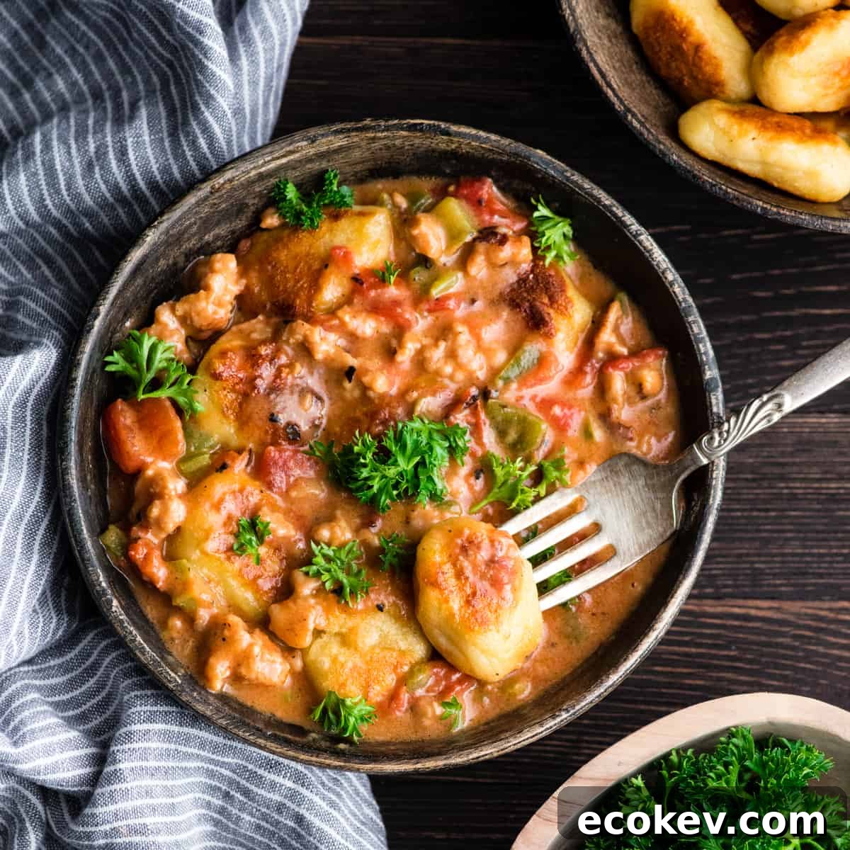 Overhead view of Cheesy Sausage Gnocchi recipe in a bowl garnished with fresh parsley with a piece of gnocchi on a fork