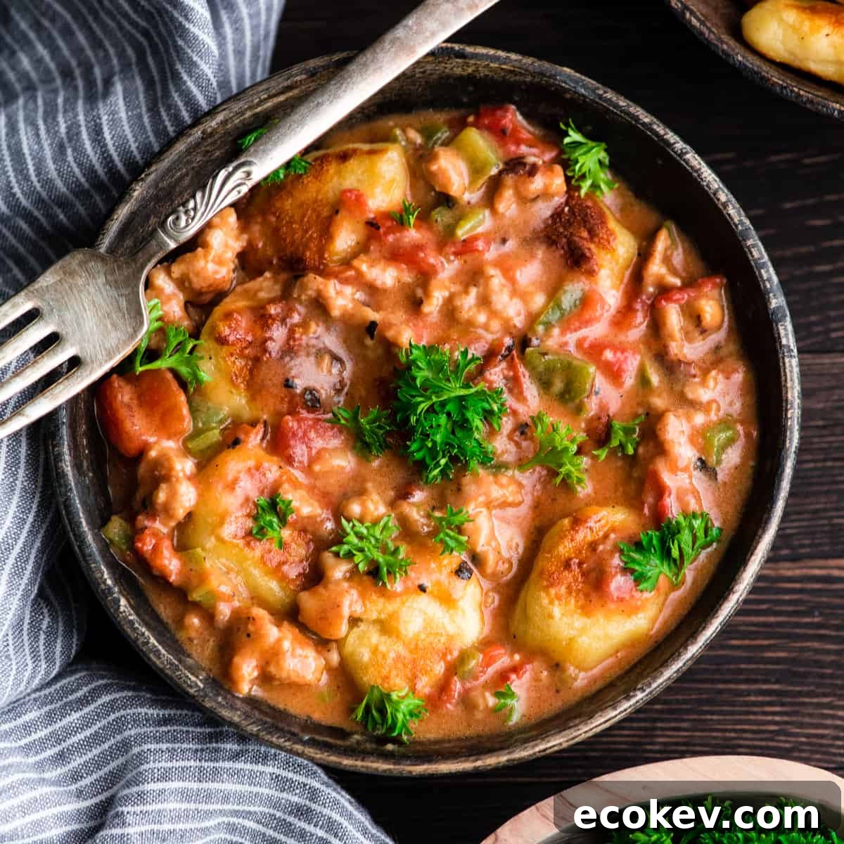 Up close overhead view of a fork with a piece of Cheesy Sausage Gnocchi on it resting on a bowl of Cheesy Sausage Gnocchi recipe