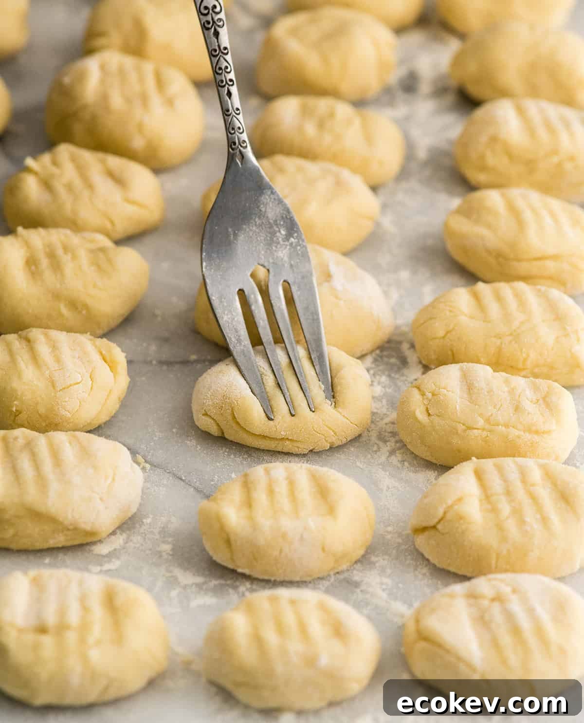 Front view of three rows of homemade potato gnocchi being pressed with a fork before cooking. 