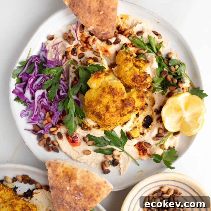 Shawarma cauliflower on a bed of hummus with pine nuts, fresh herbs, chopped cabbage and pita.