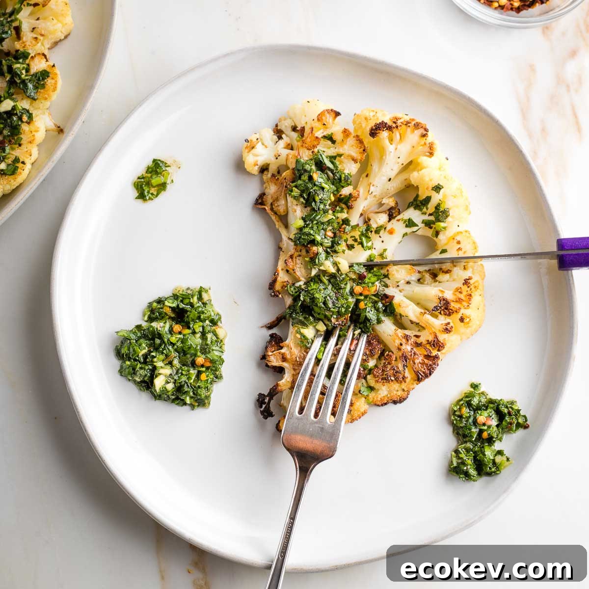 Cutting a cauliflower steak with chimichurri sauce with a steak knife.
