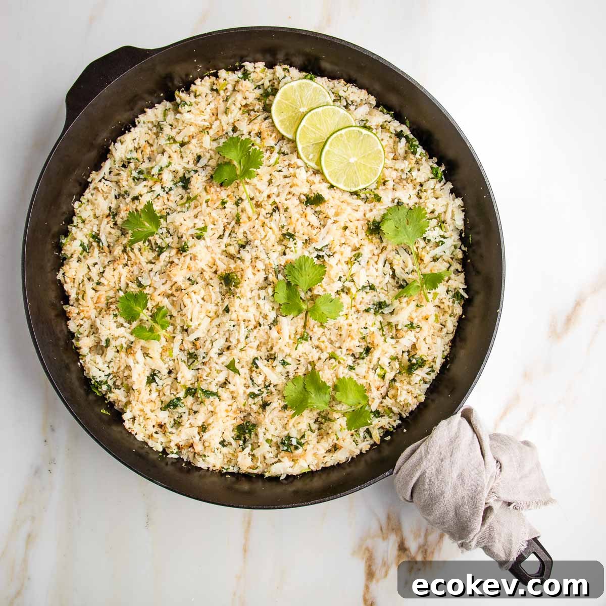 Cast iron skillet filled with cauli-rice, sprinkled with fresh cilantro and slices of limes.