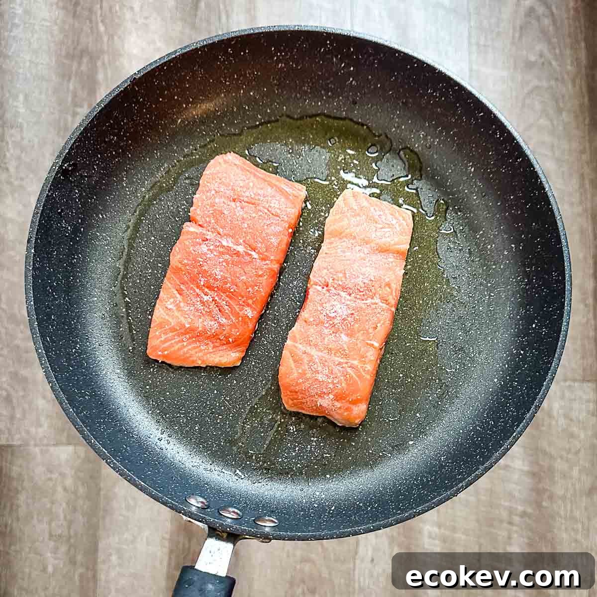 Two skin-side down salmon fillets cooking in a frying pan.