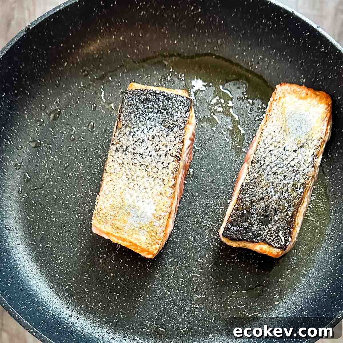 Salmon fillets are cooked skin-side up in a frying pan.