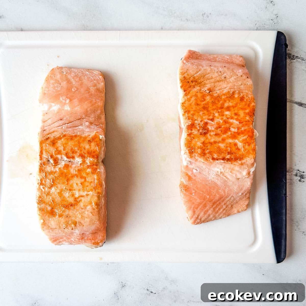 Two cooked salmon fillets on a white cutting board.