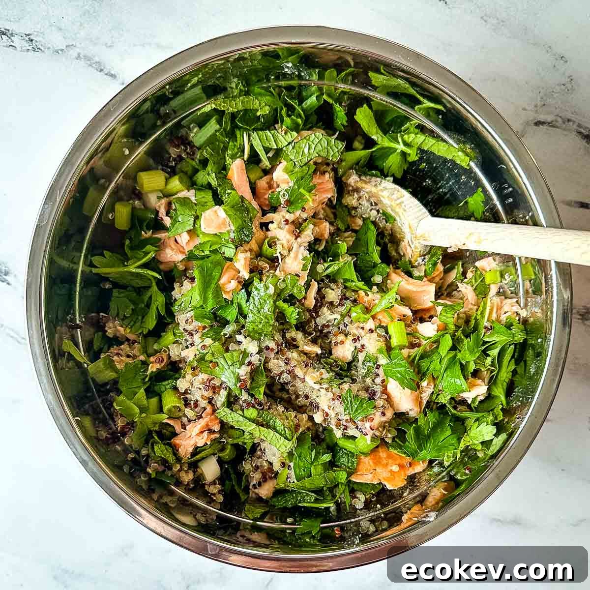 The ingredients for salmon quinoa salad are mixed together in a silver bowl.