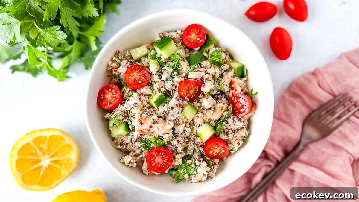 Salmon quinoa salad in a white bowl surrounded by cherry tomatoes, fresh parsley, and a cut lemon.