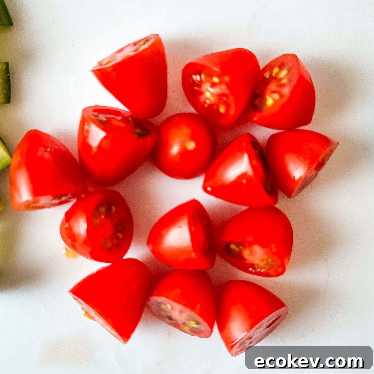 Halved cherry tomatoes on a white cutting board.