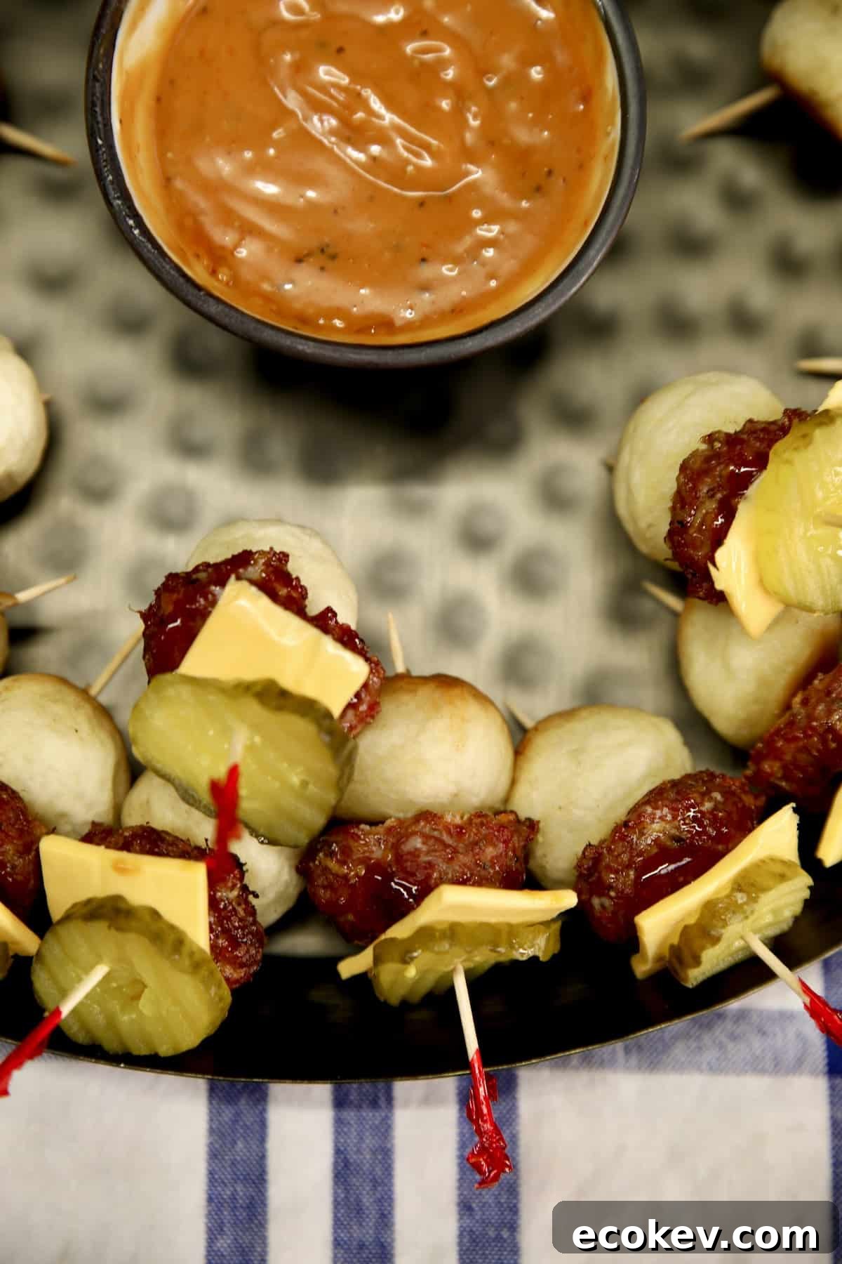 Mini cheeseburgers on a platter with sauce.