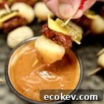 Mini cheeseburger appetizer on a toothpick, dipping into sauce.