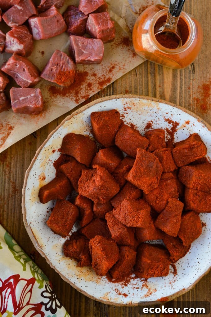 Chunks of raw sirloin steak coated with smoked paprika. Other uncoated steak sits next to it on butcher paper with a jar of smoked paprika.