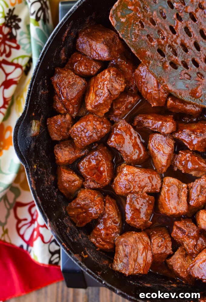 A cast iron skillet with cooked chunks of smoked paprika coated sirloin steaks next to a colorful napkin.