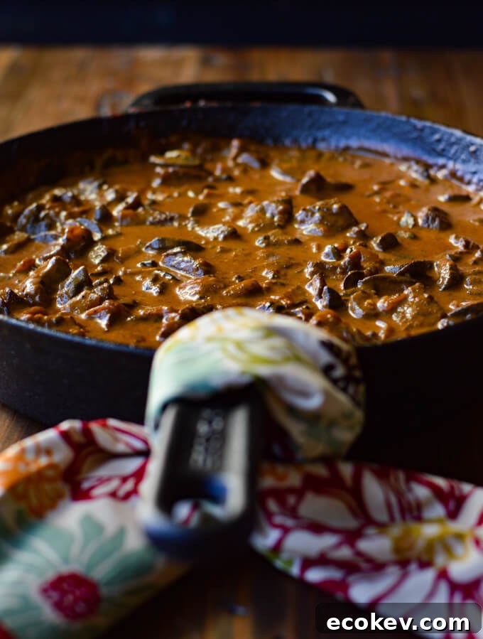 A front view of beef stroganoff in a cast iron skillet with a napkin wrapped around the handle.
