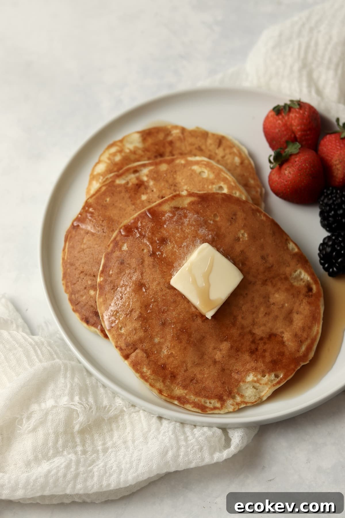 Single serve pancakes on a plate with maple syrup and berries.