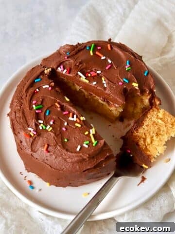 Single serve yellow cake with chocolate frosting on a small plate with a fork.