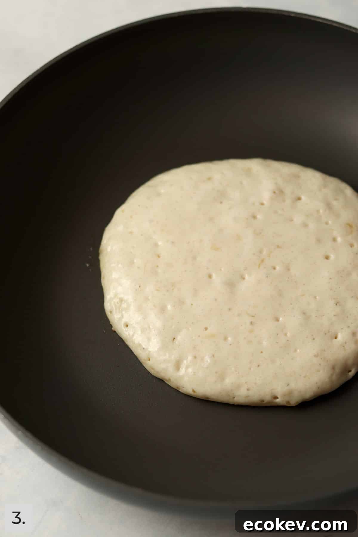 One pancake in a nonstick skillet before being flipped to show bubbles on top.