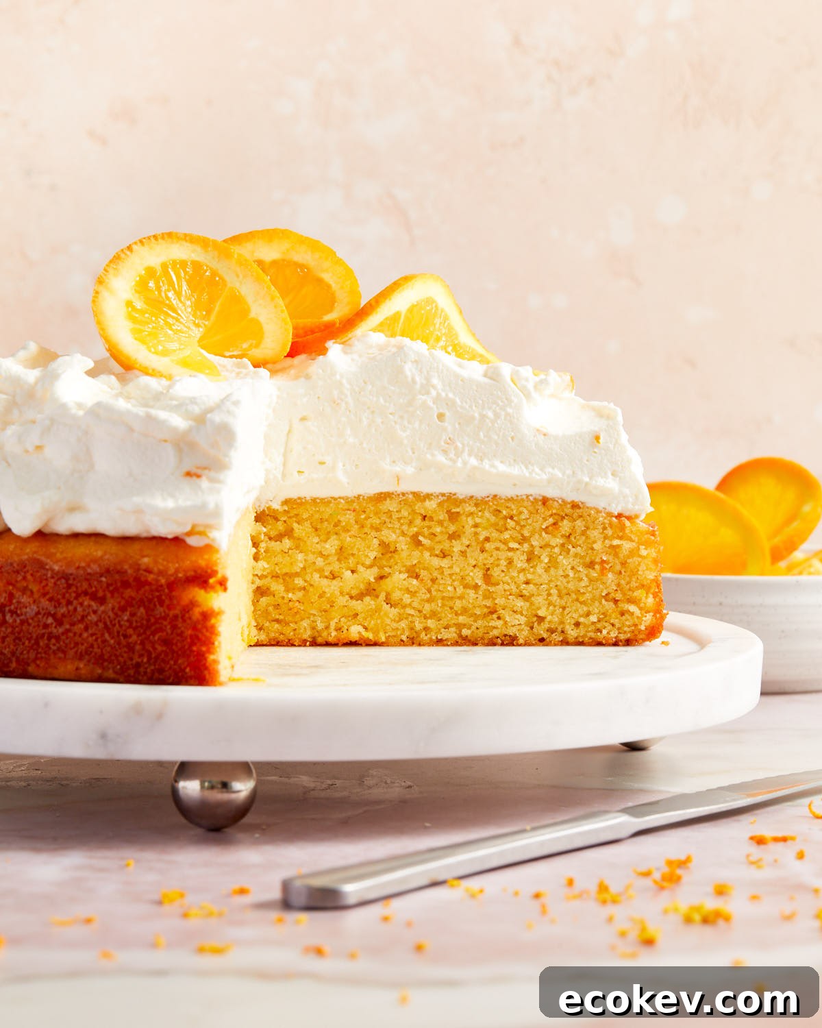 Side view of orange almond flour cake on a white cake plate with slices of cake removed.