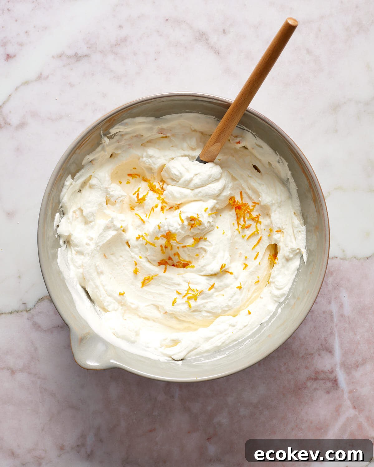 Whipped cream topping in a grey bowl with a spatula stirring in orange zest.