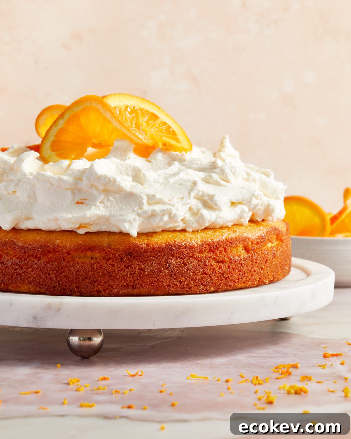 Side view of orange cake topped with whipped cream and orange slices on a white cake plate.