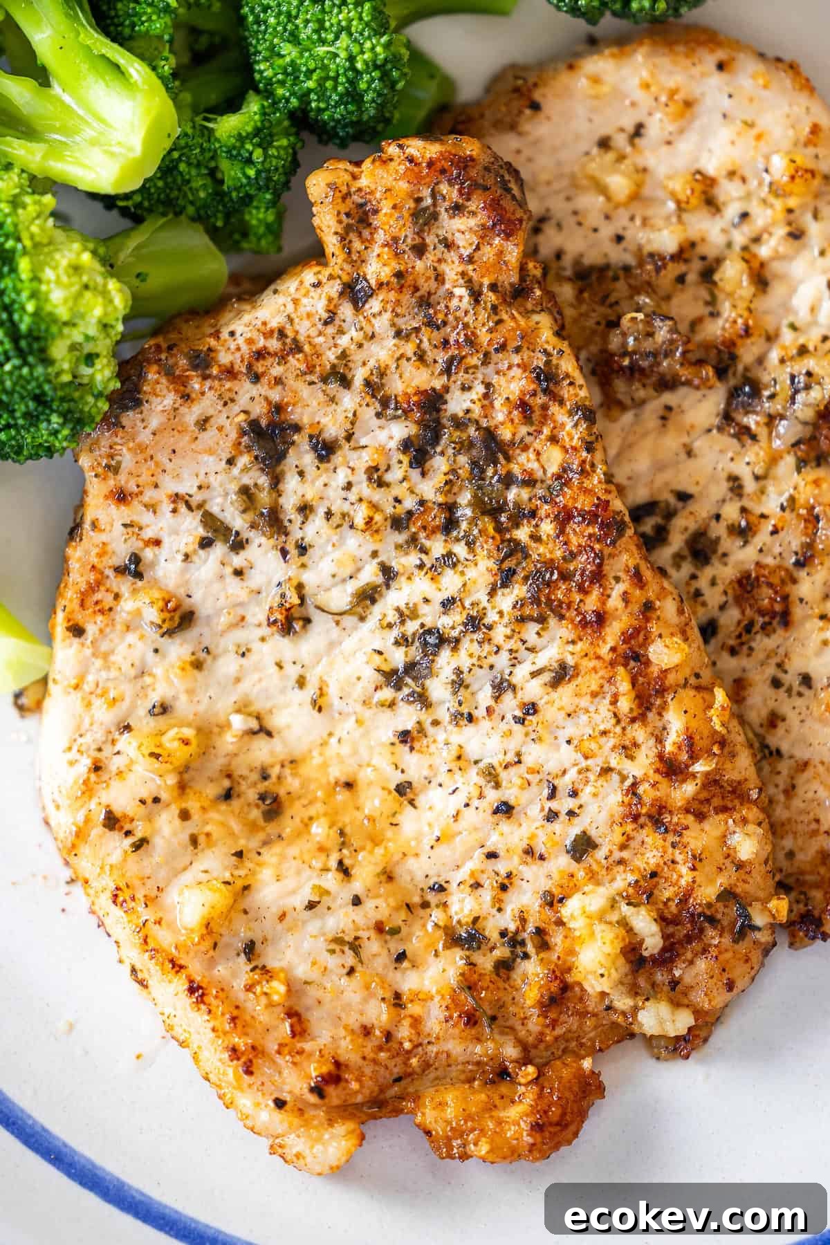 Two pan-seared pork chops seasoned with garlic, served on a plate alongside a side of steamed broccoli.