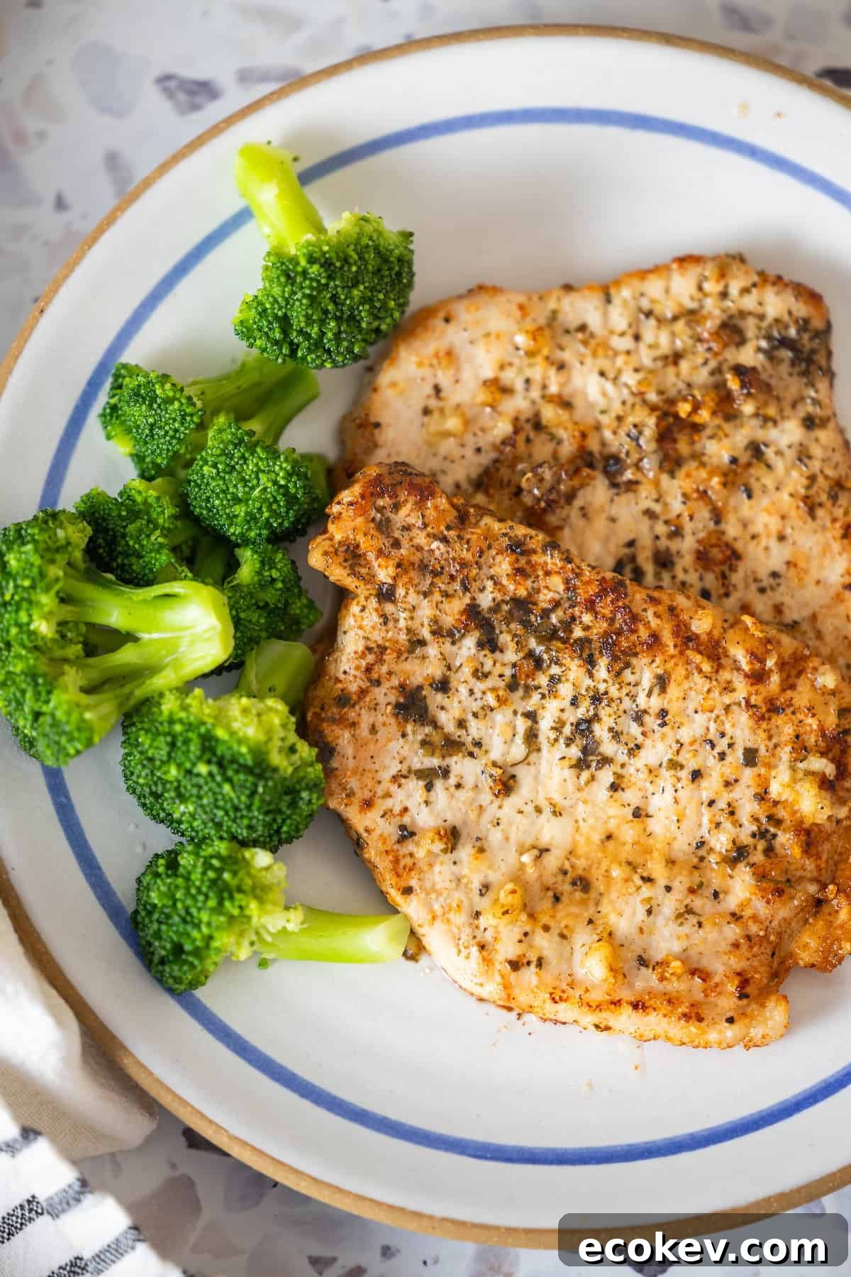 A plate with two pan-seared grilled pork chops, seasoned to perfection, and a side of steamed broccoli.