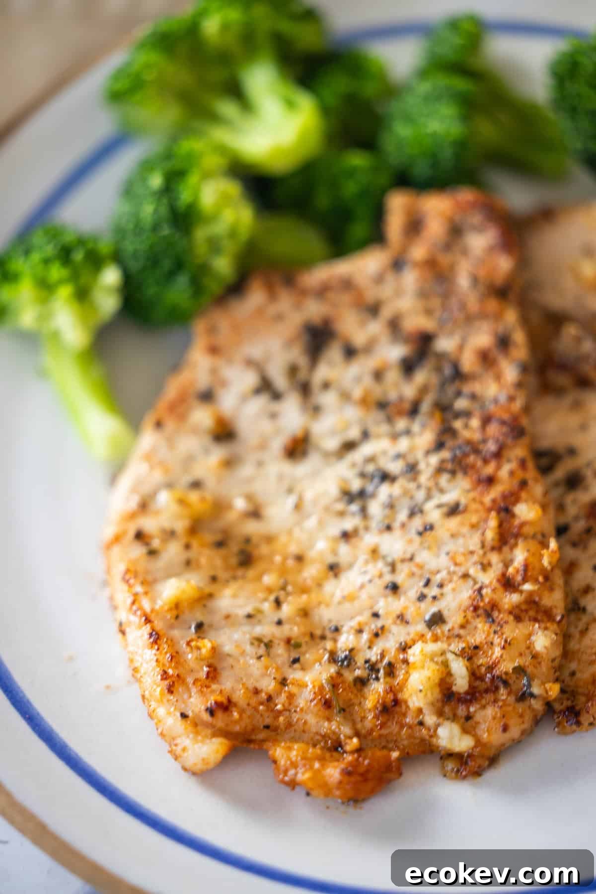 A plate with two pieces of pan-seared, seasoned chicken breast and steamed broccoli, infused with a hint of garlic.