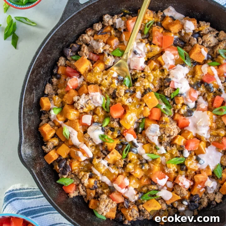 Cast iron pan with ground turkey sweet potato skillet with black beans and garnished with diced tomatoes, green onions, and a drizzle of a sauce.