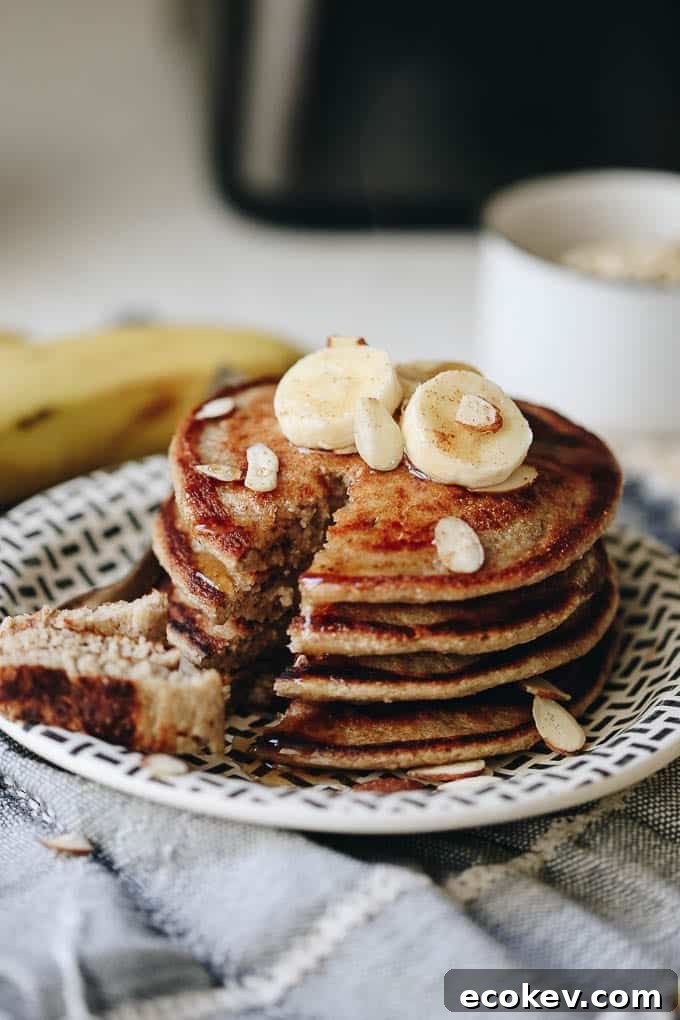 Stack of oat flour pancakes with bananas, slivered almonds and maple syrup.