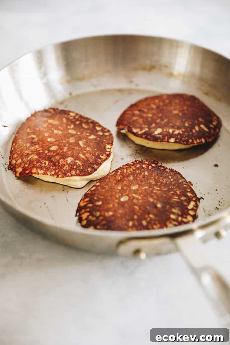 3 banana oatmeal pancakes in silver frying pan.