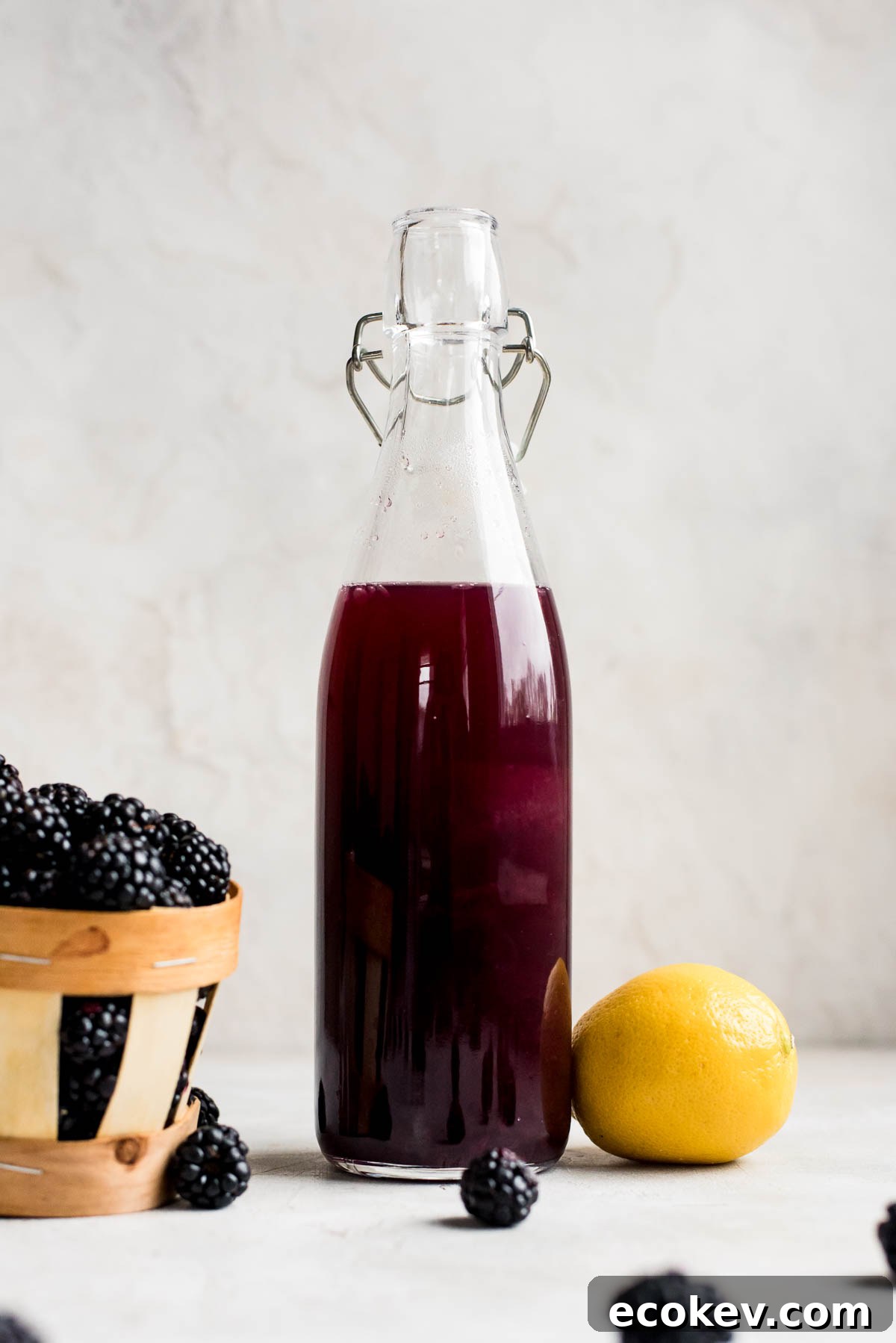 blackberry syrup in bottle next to blackberries and lemon