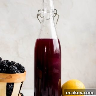 blackberry syrup in bottle next to blackberries and lemon