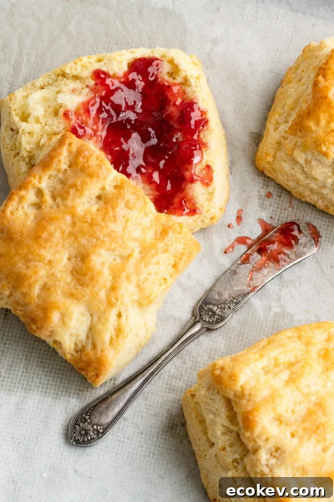 Buttermilk biscuit cut open with the bottom covered in a spread of raspberry jam on a baking pan.